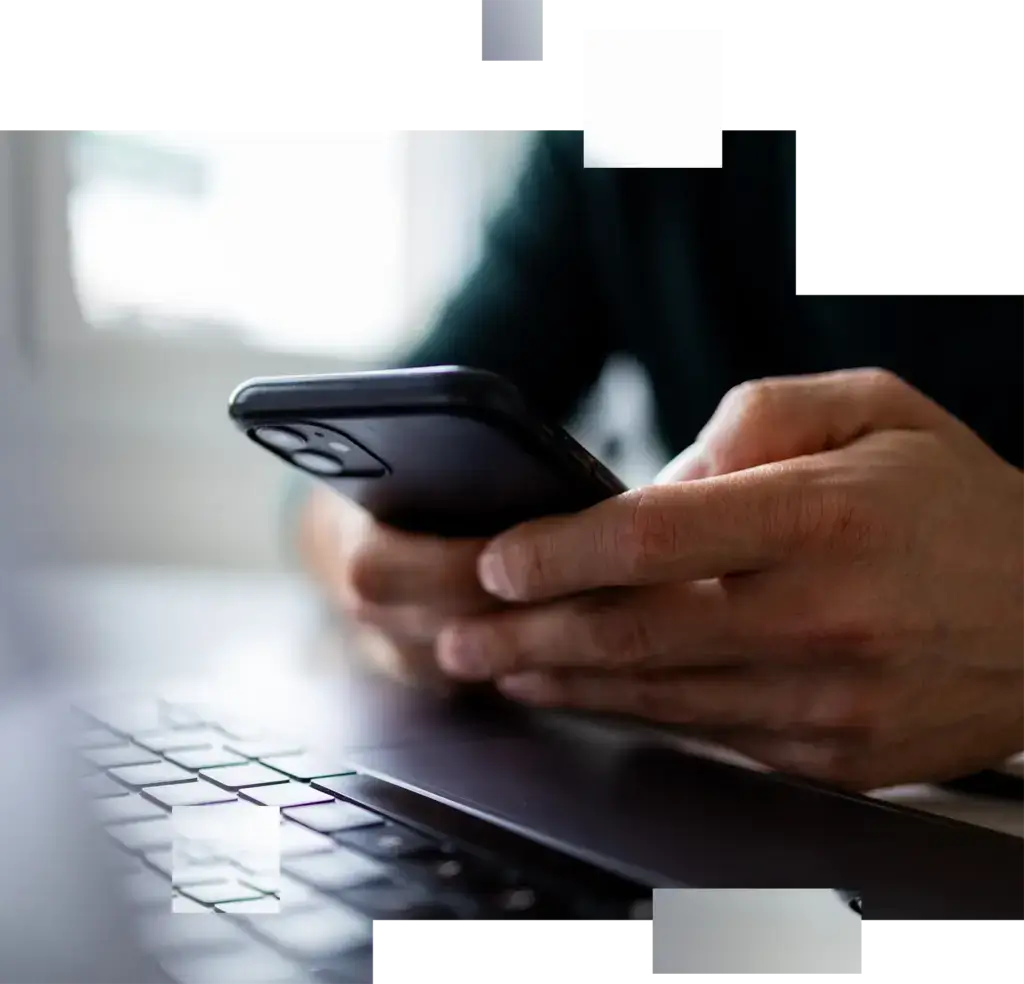 Hände halten ein Smartphone über einer Laptop-Tastatur